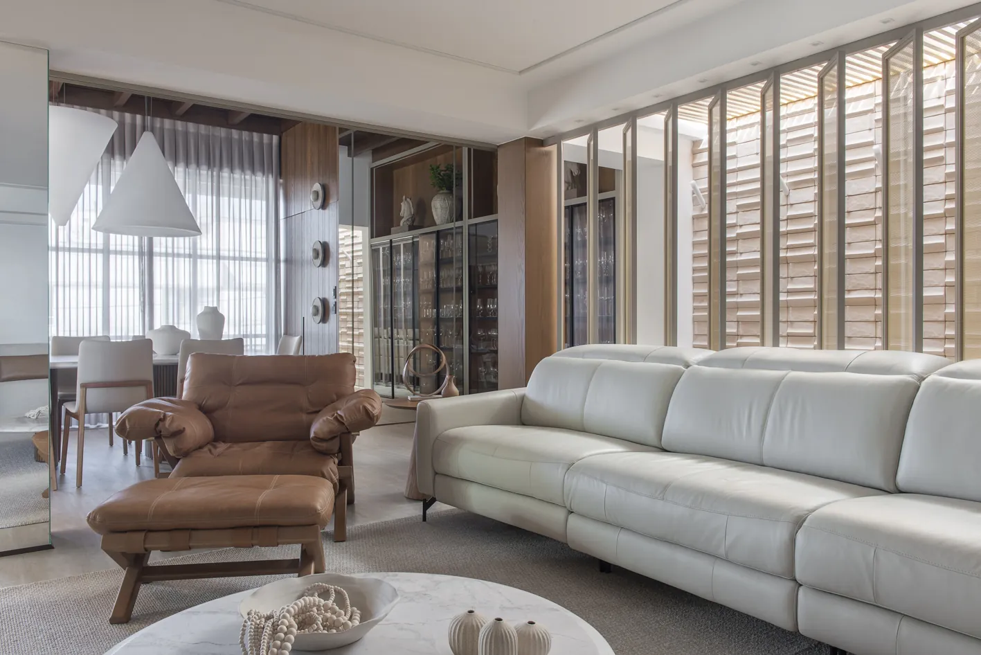 Sala de estar completa com sofá claro, poltrona de couro caramelo e mesa de centro
